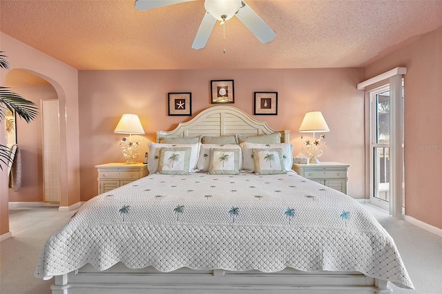 bedroom featuring arched walkways, a textured ceiling, light colored carpet, a ceiling fan, and baseboards