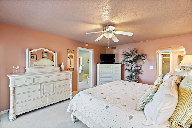 carpeted bedroom featuring ceiling fan, arched walkways, a textured ceiling, and ensuite bathroom