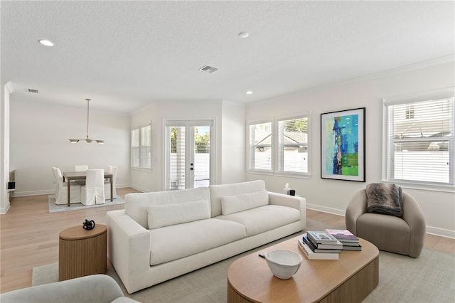 living area with light wood-type flooring, a healthy amount of sunlight, visible vents, and french doors