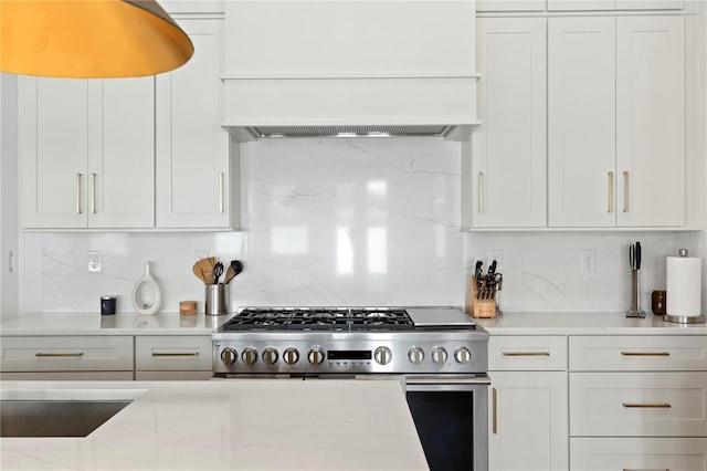 kitchen featuring stainless steel gas range oven, light stone countertops, premium range hood, white cabinetry, and backsplash