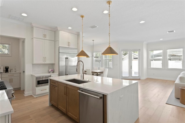 kitchen featuring an island with sink, built in appliances, light countertops, white cabinetry, and a sink