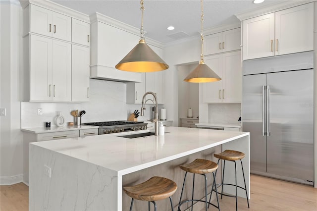 kitchen with a center island with sink, a sink, white cabinets, and stainless steel built in fridge