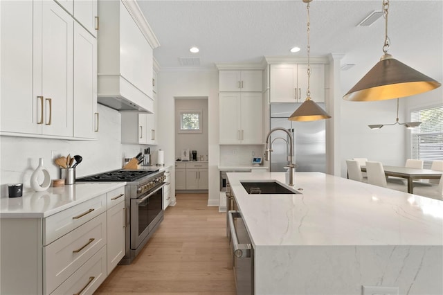 kitchen with premium appliances, pendant lighting, white cabinets, a sink, and light stone countertops