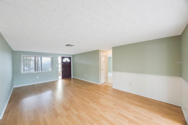 interior space with baseboards, visible vents, a textured ceiling, and light wood finished floors