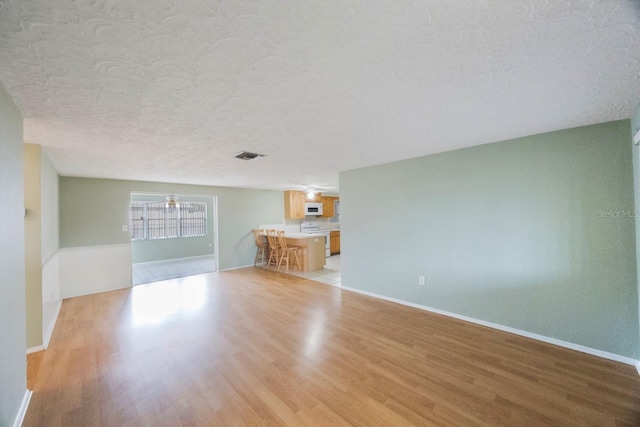 unfurnished living room featuring baseboards, visible vents, a textured ceiling, and light wood finished floors