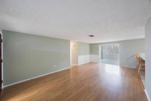 spare room with visible vents, a textured ceiling, baseboards, and wood finished floors