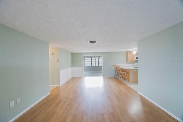 unfurnished living room featuring light wood-style floors, baseboards, visible vents, and a textured ceiling