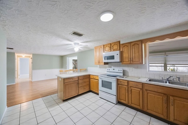 kitchen with light countertops, visible vents, a sink, white appliances, and a peninsula