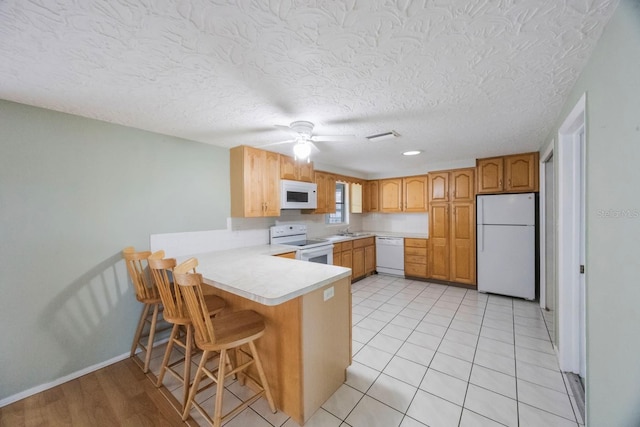 kitchen with light countertops, brown cabinetry, white appliances, a peninsula, and a kitchen breakfast bar