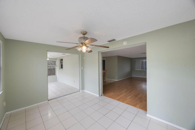 empty room featuring ceiling fan, visible vents, baseboards, and light tile patterned flooring