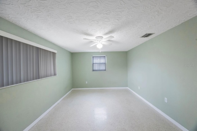 empty room with a textured ceiling, speckled floor, visible vents, baseboards, and a ceiling fan