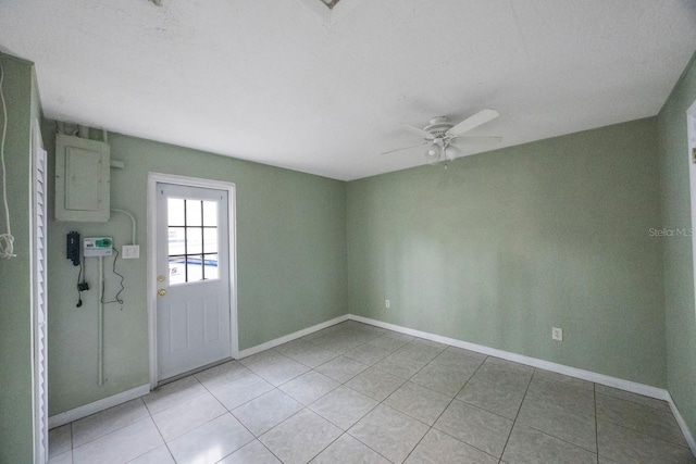 empty room featuring light tile patterned floors, ceiling fan, electric panel, and baseboards