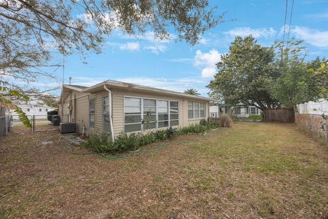 rear view of property with a lawn, cooling unit, and fence