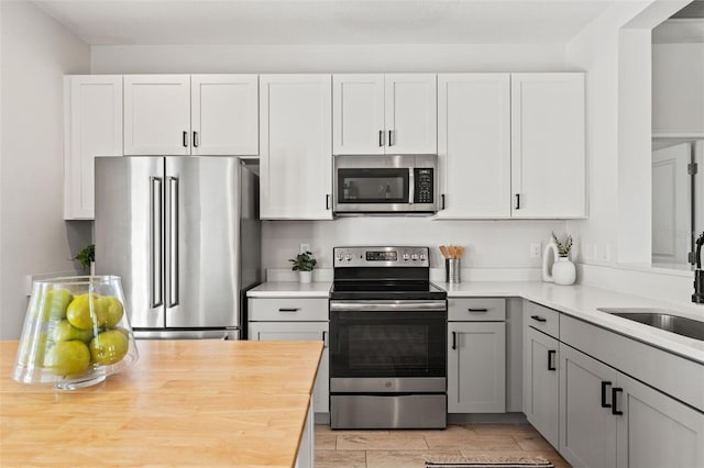 kitchen with gray cabinetry, butcher block counters, a sink, white cabinetry, and appliances with stainless steel finishes