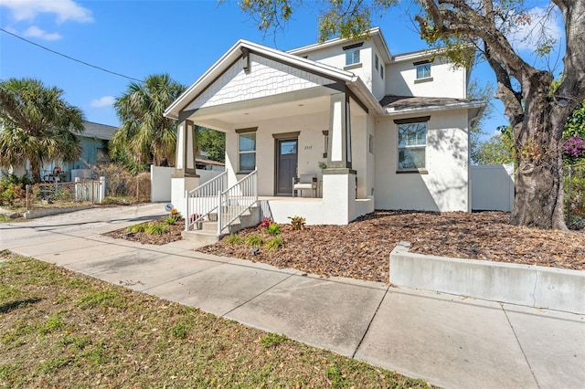 view of front facade featuring covered porch, fence, and stucco siding