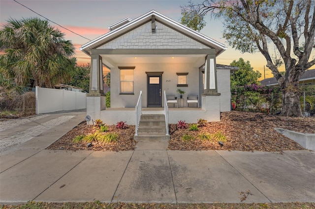 bungalow-style house featuring a porch, a fenced front yard, and stucco siding