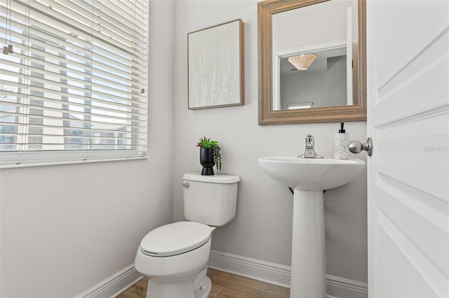 half bathroom featuring toilet, a sink, baseboards, and wood finished floors