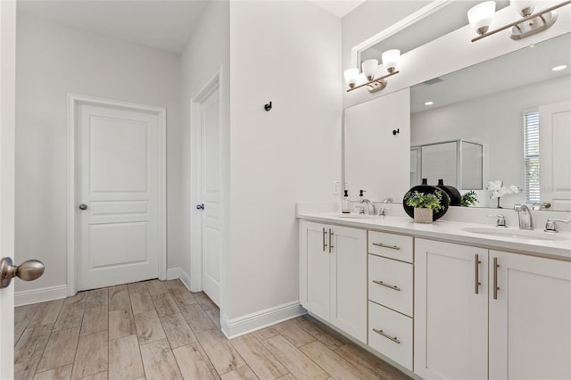 bathroom with double vanity, baseboards, wood finished floors, a shower stall, and a sink