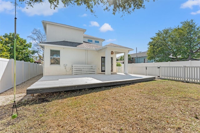 rear view of property featuring a fenced backyard, a yard, a deck, and stucco siding