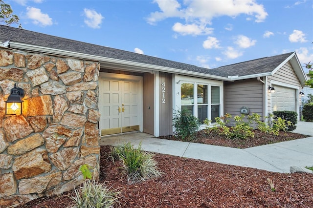 entrance to property with an attached garage and a shingled roof