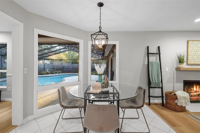 dining room with an inviting chandelier, light tile patterned floors, baseboards, and a lit fireplace