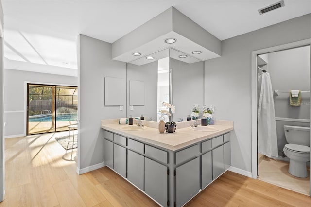 full bathroom featuring visible vents, toilet, a sink, wood finished floors, and double vanity