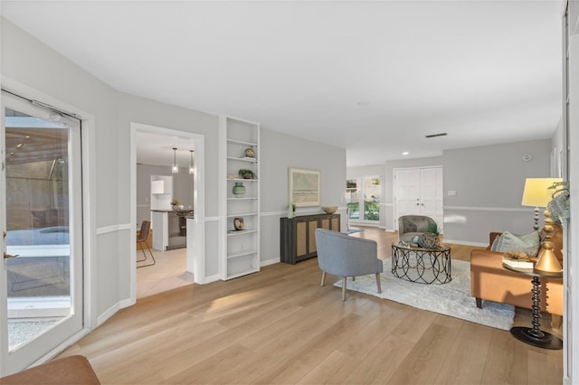 living room featuring visible vents, light wood-style flooring, and baseboards