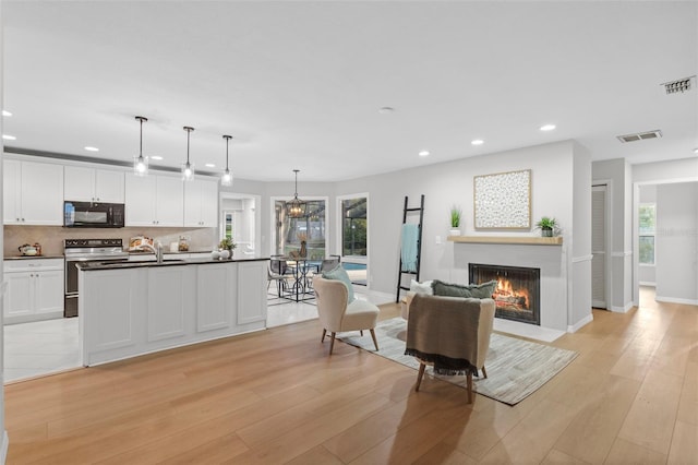 living room featuring recessed lighting, visible vents, a fireplace with flush hearth, and light wood-style floors