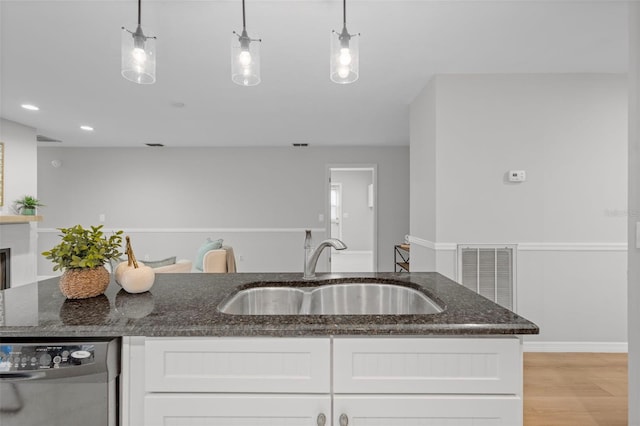 kitchen with dark stone countertops, visible vents, a sink, white cabinets, and stainless steel dishwasher