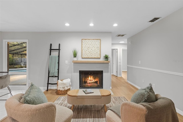 living room featuring recessed lighting, baseboards, a warm lit fireplace, and light wood-style flooring