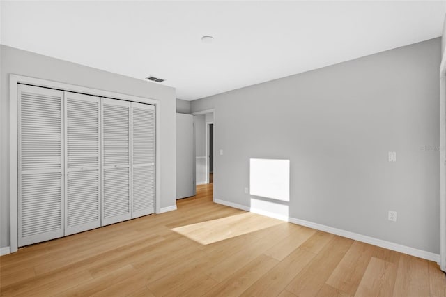 unfurnished bedroom featuring light wood finished floors, visible vents, a closet, and baseboards