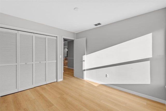 unfurnished bedroom with visible vents, baseboards, light wood-style floors, and a closet