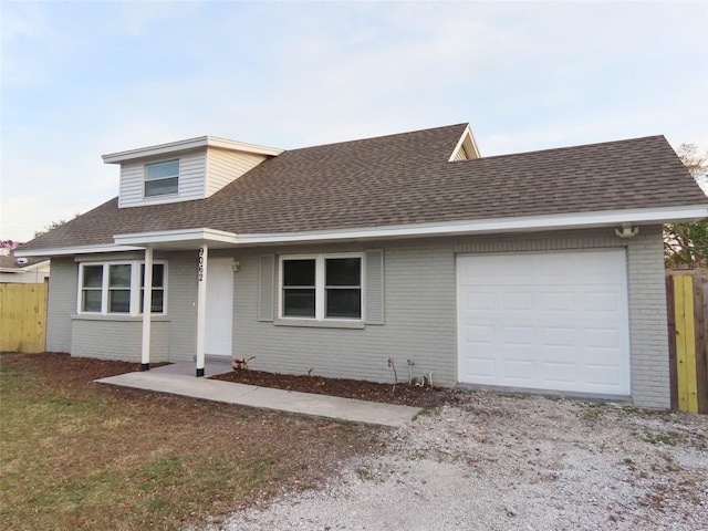 view of front of house featuring a garage, brick siding, roof with shingles, and fence