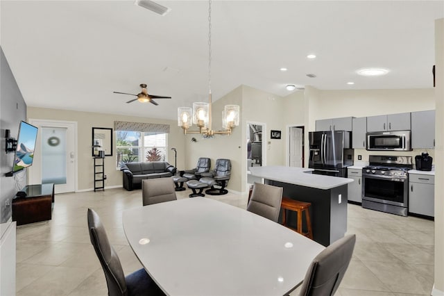 dining room with light tile patterned floors, visible vents, vaulted ceiling, baseboards, and ceiling fan with notable chandelier
