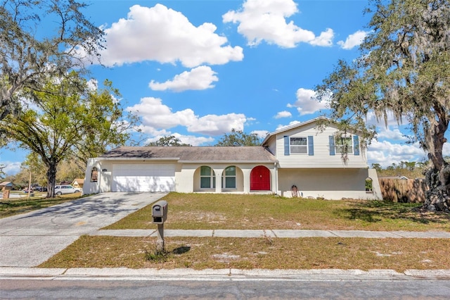 tri-level home featuring an attached garage, driveway, a front yard, and stucco siding