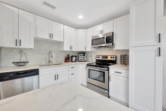 kitchen with light stone counters, stainless steel appliances, a sink, visible vents, and white cabinetry