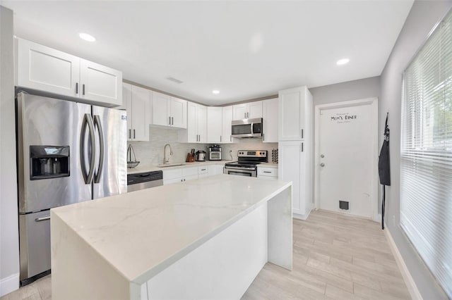 kitchen with tasteful backsplash, white cabinets, light stone counters, stainless steel appliances, and a sink