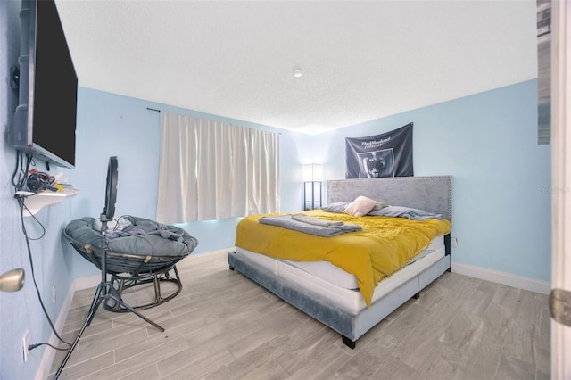 bedroom with a textured ceiling, baseboards, and wood finished floors