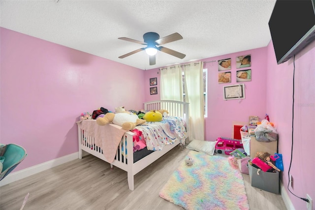 bedroom with a ceiling fan, a textured ceiling, baseboards, and wood finished floors