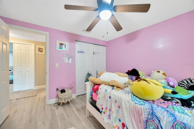 bedroom featuring a closet, light wood-style floors, ceiling fan, a textured ceiling, and baseboards