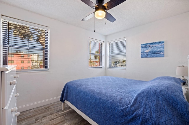 bedroom with multiple windows, a textured ceiling, baseboards, and wood finished floors