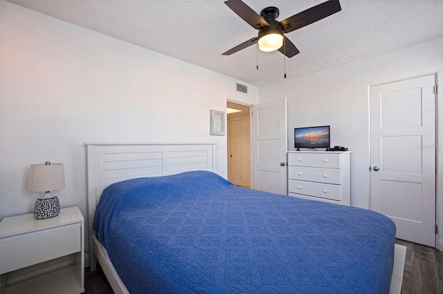 bedroom featuring a textured ceiling, dark wood finished floors, visible vents, and a ceiling fan