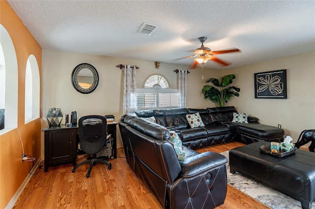 living room featuring a textured ceiling, ceiling fan, visible vents, baseboards, and light wood-style floors