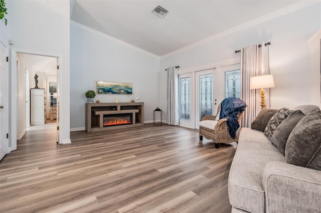 living area featuring ornamental molding, a glass covered fireplace, vaulted ceiling, wood finished floors, and baseboards