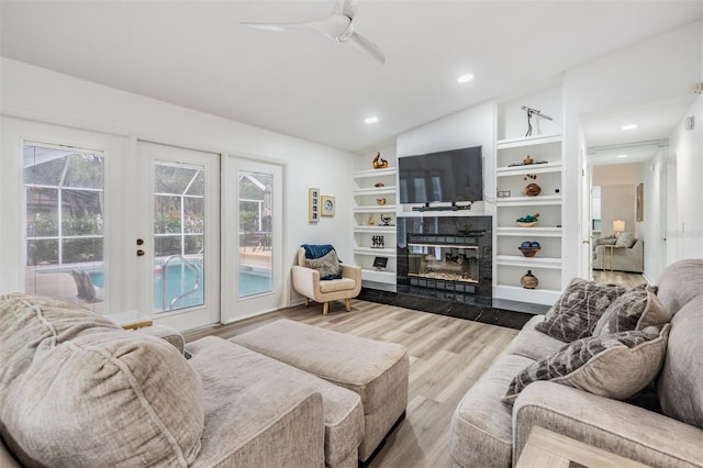 living area with a tile fireplace, recessed lighting, wood finished floors, built in features, and vaulted ceiling