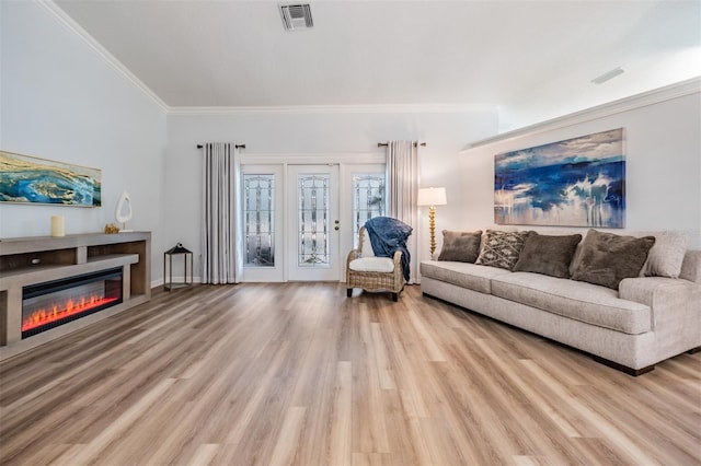 living room with ornamental molding, a glass covered fireplace, visible vents, and light wood finished floors