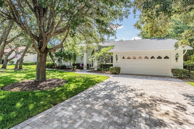 view of front facade with a garage, decorative driveway, a front lawn, and stucco siding