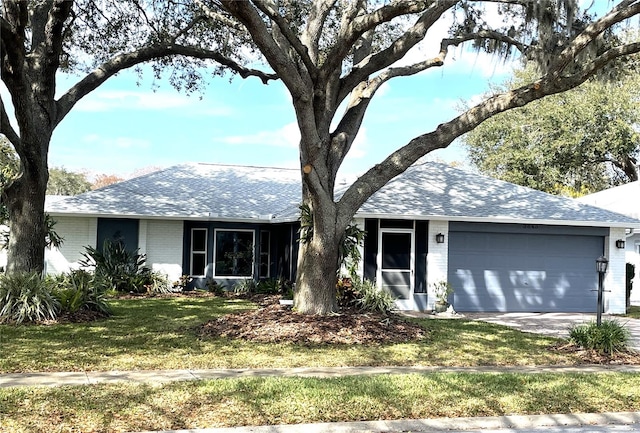 ranch-style home with brick siding, roof with shingles, concrete driveway, an attached garage, and a front yard