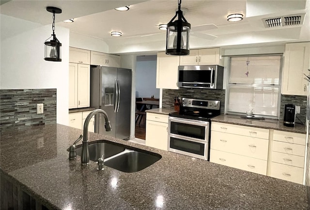 kitchen with visible vents, appliances with stainless steel finishes, dark stone countertops, a sink, and backsplash