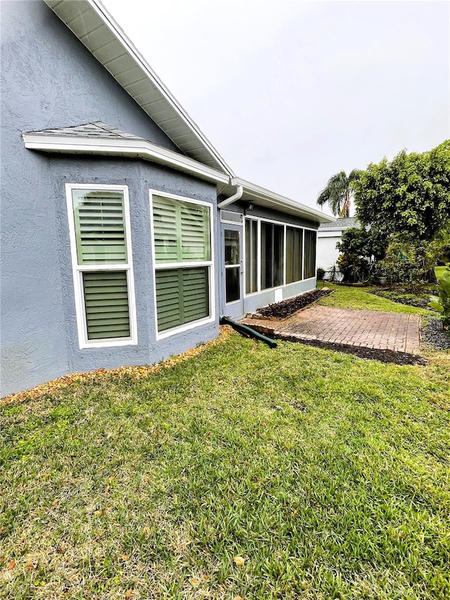 exterior space featuring a yard, a sunroom, and stucco siding